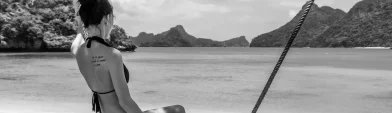 Woman sitting on a swing at a beach in Thailand with ocean and limestone cliffs